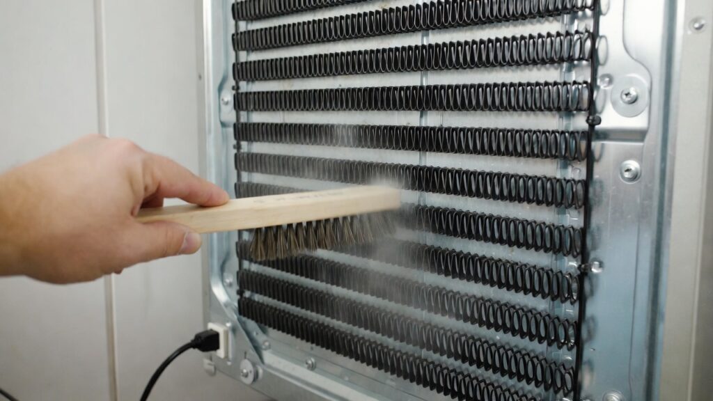 Cleaning dust from black refrigerator condenser coils.